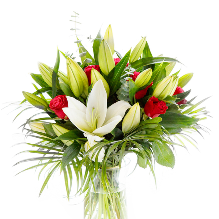 A refined, studio-styled bouquet that reads as both intimate and ceremonious: a solitary, fully open creamy-white Oriental lily dominates the centre, its satin-smooth petals curving slightly to expose delicate pale yellow stamens and a pale green pistil. Encircling this focal bloom are numerous lily buds in soft lime-green and creamy yellow tones-some tightly closed, some teasingly ajar-giving the arrangement a sense of life in progress. Scattered through this pale palette are several velvety red rosebuds and small roses, their petals still mostly curled, introducing concentrated pockets of passionate colour that contrast beautifully with the lilies. The greenery is thoughtfully layered: glossy, deep forest-green leaves form a supportive backdrop; elongated, feather-like palm fronds in an emerald shade cascade gently to add movement and sculptural interest; and silvery-green eucalyptus stems with round leaves punctuate the bouquet with cool, aromatic texture. All stems are arranged in a plain, cylindrical clear glass vase so the pale green stems are visible beneath the fresh water, a simple detail that keeps the focus on botanical form and freshness. Shot against a bright white background, the bouquet's tones-soft ivory, lime, vivid red, and layered greens-read clearly and with emotional clarity. As a local florist familiar with Oxford's rhythms near the Botanic Garden and High Street, I imagine this piece arriving as a thoughtful anniversary gift or a tasteful centrepiece for a celebratory meal, delivering both the lilies' honeyed sweetness and the roses' deeper, romantic warmth-available for same-day delivery across central Oxford when freshness matters most. Flowers Oxford crafts arrangements like this with attention to scent, season, and the quiet language of flowers.
