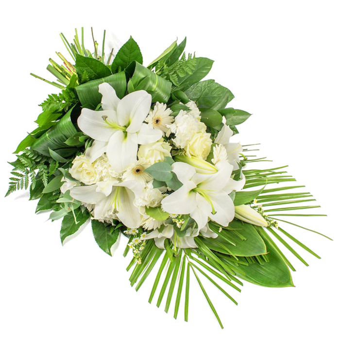 This long, teardrop-style funeral spray is photographed against a clean white background, its elongated diagonal form suggesting a gentle cascade of white blooms over a bed of rich foliage. The main focus is a collection of large white lilies, their trumpet-shaped flowers fully open in some places, revealing softly curved petals and central stamens dusted with pale pollen, while other stems hold perfectly formed buds, still closed and serene. Intertwined among the lilies are clusters of velvety white roses, from tightly furled buds to partially open flowers that show layers of delicately spiralled petals. Smaller, daisy-like white Gerbera blooms with pale yellow or cream centres are tucked throughout, adding a light, cheerful note to the otherwise tranquil palette. Tiny sprigs of white filler flowers, akin to gypsophila or waxflower, provide a fine, airy texture, bridging the spaces between the larger blooms. The arrangement is framed and shaped by an abundant mix of greenery: broad, glossy leaves fold and overlap to create structure, feathery fern fronds lend softness, and rounded eucalyptus leaves add cool, muted tones. From the lower right corner, slim palm fronds fan outward in a graceful arc, emphasising the cascading, flowing shape and giving the spray a contemporary edge. The overall impression is one of quiet dignity and heartfelt sympathy, ideal as a memorial tribute or funeral arrangement for services around Oxford, whether placed in a tranquil church near Summertown, at a crematorium on the outskirts of the city, or delivered to a family home in Jericho as a message of peace and remembrance.