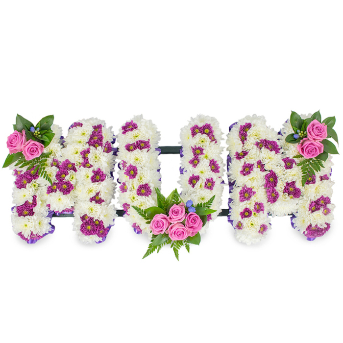 Set against a plain white backdrop, this heartfelt floral tribute forms the word MUM in large, three-dimensional capital letters, each letter built from a dense cushion of pristine white chrysanthemums that give the surface a plush, almost textile-like quality. Interspersed across the white base are thoughtful patches of magenta and deep purple spray chrysanthemums that add contrast and a gentle patterned effect, while delicate purple ribbon edges trace the letters in a subtle outline, enhancing their clarity and softness. Three clusters of bright pink spray roses punctuate the design: a slender grouping at the upper left of the first M, a mirrored cluster at the upper right of the final M, and a fuller, more prominent bouquet of several pink roses nestled into the lower curve of the central U. Rich green foliage - fern fronds and varied leaves - fans around these rose clusters, giving weight and natural movement, and tiny blue accent flowers appear as delicate highlights between petals. A thin, dark horizontal bar runs behind the letters, holding the trio together and giving the impression of a carefully framed memorial piece. The arrangement is lit with soft, even light that reveals the chrysanthemums' dense texture and the roses' tender unfolding petals; there is the faint, clean scent of fresh blooms. This bespoke piece reads as a dignified sympathy tribute, suited to funeral services or wakes in Oxford venues from Christchurch Meadows chapels to smaller parish services, conveying tenderness, respect and remembrance.