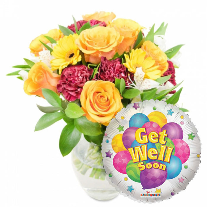 A warm, uplifting Get Well Soon arrangement presented simply against white: a voluminous bouquet in a clear glass vase paired with a gleaming Mylar balloon, composed to reassure and cheer. The floral story begins with several large, unfolding roses in warm orange and deep yellow that form a soft, sunlit centre; their petals are plush and slightly scented, inviting a reassuring breath. Bright yellow gerbera daisies fan outward like small suns, their solid colour and dark centres creating immediate optimism, while rich maroon or burgundy carnations introduce a layered, ruffled texture that deepens the composition. Sprays of petite white alstroemeria are woven among the larger blooms, offering points of light and a delicate, airy counterpoint. Lush green foliage-varied leaf shapes and glossy finishes-frames the bouquet, and the stems and water are visible through the clear vase, signalling freshness and thoughtful conditioning. To the lower right, overlapping the bouquet, a round silver foil balloon catches the light; its centre shows a playful cluster of cartoon balloons in bright purple, sky blue, lime green, hot pink and sunny yellow, some printed with stripes, polka dots or checkerboards. Prominent yellow-and-blue lettering proclaims Get Well Soon with a subtle shadow for dimension, while small starburst graphics rim the balloon's white edge and a tiny Kaleidoscope logo sits at the base. The arrangement reads as both comforting and hopeful-suitable to send to a recovering friend or relative across Botley Road, Headington or near University Parks.