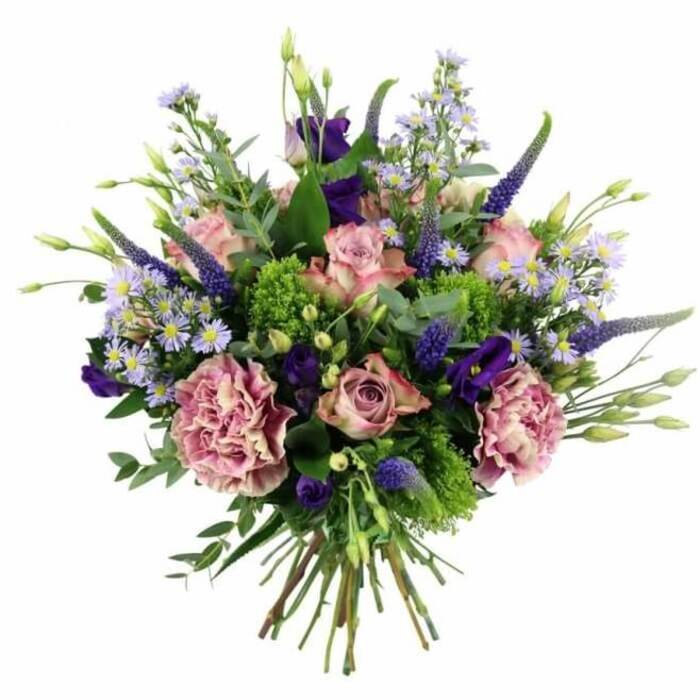 This photograph presents a sumptuous, professionally arranged bouquet on a pure white background, allowing every shade of pink, purple, and green to sing. The composition is rounded and full, with a generous cluster of pastel pink roses forming the focal point. Some roses are tightly furled, promising to open further, while others have already unfurled into open, cupped blooms that reveal intricate spirals of petals tinged with slightly deeper pink at the centres. Interlaced among the roses are voluminous carnations in dusty rose and mauve, each one a swirl of finely ruffled petals that look almost feather-soft to the touch. Rising confidently above and between these rounder shapes are elongated, tapering stems of Veronica in deep violet-blue, their slender, textured spikes giving vertical rhythm and a slightly wilder, garden-border feeling, much like the planting in the quieter corners of the Oxford Botanic Garden. Nestled lower in the arrangement, rich purple lisianthus flowers add satiny, bell-shaped depth, while scatterings of tiny, star-shaped aster-like blossoms in lavender and periwinkle create a gentle, cloud-like haze through the bouquet. The entire design is cradled by an assortment of greenery: bright, lime-green textural filler, perhaps bupleurum or green trick dianthus, punctuates the arrangement with lively sparks of colour, balanced by flatter, silvery-green eucalyptus leaves and other foliage that provide structure and a soft, herbal note. The hand-tied stems are visible at the base, neatly aligned and freshly cut, suggesting readiness for a vase on a dining table in Headington or a desk near Oxford station. The overall impression is of a luxurious, thoughtfully crafted bouquet that feels perfect for marking milestones, sending thanks, or expressing affection across the city.