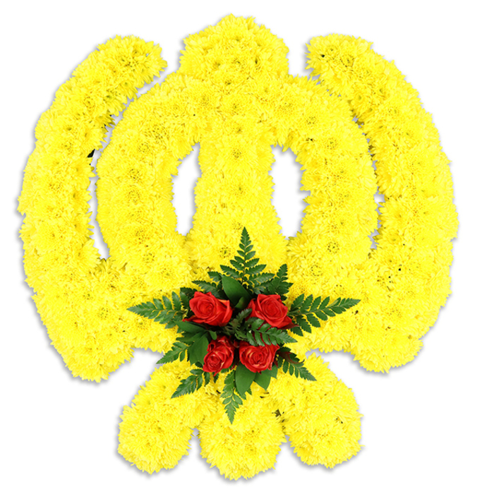 Dominating the white field of the photograph is a large, reverent floral Khanda, fashioned with the exacting eye of a specialist florist into the sacred Sikh emblem. Thousands of compact, bright yellow chrysanthemum heads are arranged to follow the emblem's sweeping arcs and points: the round chakkar reads luminous and defined, the central double-edged khanda rises in a clean vertical line, and the pair of kirpans curve decisively at the base. The texture created by the tiny, overlapping petals is soft yet sculptural, catching soft light and creating subtle shadows that emphasise depth and craftsmanship. Nestled at the converging point, a small but potent cluster of deep red roses - tightly budded and richly coloured - forms the visual and emotional centre. Those roses rest within a nest of dark green fern fronds whose fine blades provide contrast in both tone and surface, framing the red against the dominant yellow. Visually, the piece communicates solemnity and respect; olfactorily, the composition offers a gentle floral bouquet with green, powdery chrysanthemum notes and the fuller, classic scent of roses. Intended for solemn occasions or to mark cultural remembrance, this floral Khanda would be welcomed at services throughout Oxford - from memorials in Headington to cultural ceremonies around the city's university chapels - where its clean, symbolic presentation and expert construction convey care, tradition and quiet dignity.