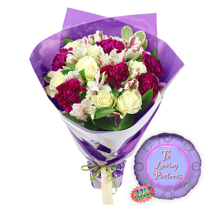 Against a bright white backdrop, a thoughtfully arranged romantic bouquet stands as the focal point, paired with a small celebratory balloon that adds a playful, affectionate note. The bouquet is lush yet carefully balanced, built around several creamy white roses whose petals are still mostly furled, forming tight, spiralled hearts that suggest fresh, enduring love. Intertwined among them are rich magenta and burgundy carnations, their densely ruffled petals forming pillowy clusters that bring intensity and drama, much like the deep hues of Oxford's college robes. Delicate white alstroemeria, also known as Peruvian lilies, peek through the fuller blooms, each blossom marked with fine reddish-brown stripes and speckles on the inner petals that add intricate texture and visual interest. A generous collar of greenery surrounds the flowers, with glossy green leaves and touches of variegated foliage softening the edges and adding a natural, garden-fresh feel, as if gathered from a well-kept courtyard off St Giles'. The bouquet is wrapped in a two-layered presentation: an inner layer of crisp white paper that gives structure and a modern, clean line, and an outer layer of sheer, crinkled purple cellophane that rises around the blooms like soft waves, catching reflections of light. The stems at the base are held firmly together by a narrow bright green satin ribbon, tied into a tidy bow, with a small, rectangular light brown gift tag dangling from the knot, ready for a handwritten message from one partner to another. To the right of the bouquet rests a round metallic purple foil balloon with a distinctive scalloped, rosette-like edge. In its centre, on a lighter lilac background, the words To Loving Partners appear in pretty, flowing pink script. A small rainbow-effect holographic sticker near the edge hints at a shimmering finish, making this combination of flowers and balloon a fitting romantic gift for anniversaries, Valentine's surprises, or special evenings in Oxford, whether near Christ Church Meadow or along Banbury Road.
