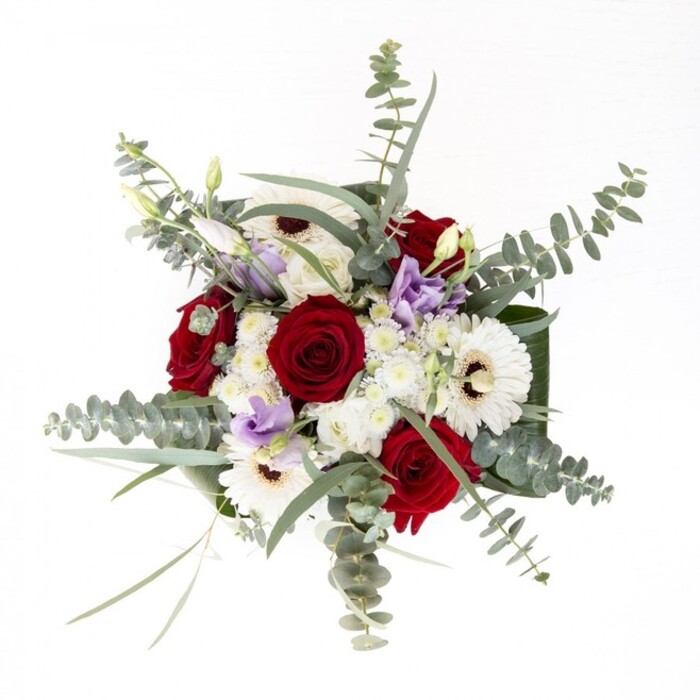 As an Oxford florist, I see this bouquet as a harmonious blend of heritage and contemporary style-each flower distinct, yet all unified in quiet splendour. Majestic red roses unfurl alongside creamy white gerberas, their petals a visual echo of Oxford's iconic collegiate whites, while deep espresso-brown centres anchor the composition with subtle warmth. Between them, pastel lisianthus, some still coyly in bud, offer a gentle transition of colour, like a soft lavender sunset seen from Port Meadow. Clusters of tiniest white filler flowers act as ethereal accents, adding cloudlike volume and balancing the arrangement's structure. Eucalyptus leaves, their cool, silvery hue reminiscent of early morning mist along the river, arc gracefully overhead, infusing the bouquet with a touch of woodland freshness and aromatic complexity. Encasing the bouquet, broad green leaves add polish and weight, their glossy surfaces catching the gentle Oxfordshire light that pours through a nearby window. The stems, elegantly contained in a transparent glass vase, remain visible-submerged in sparkling water that proclaims their freshness. Whether marking a golden anniversary, sending comfort to a friend on Banbury Road, or welcoming someone new to the city, this arrangement reflects a love of natural beauty and the refined skill characteristic of Oxford's finest florists.
