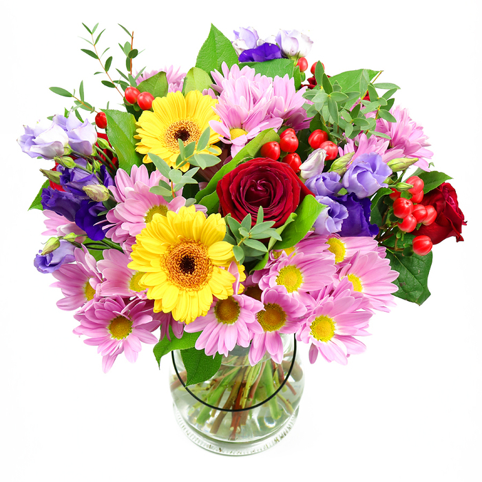A vibrant mixed bouquet, displayed in a clear glass vase against a crisp white background, radiates the same welcoming spirit you might feel walking past independent florists near Oxford's Cowley Road. At its centre, velvety red roses open into generous spirals, offering a deep, romantic hue that grounds the design. Close by, two bright yellow gerbera daisies lift their wide, open faces, each one featuring a distinctive dark brown-orange centre that adds character and visual interest. Encircling these main blooms is a generous halo of soft pink daisy-like chrysanthemums, their many fine petals and sunny yellow centres creating a light, airy texture that seems almost cloud-soft. Winding in and out of this pastel cushion, stems of lisianthus in serene purple and lavender shades introduce cooler tones; their bell-shaped flowers and slim, twisting stems lend elegance and subtle movement, as if caught in a gentle breeze. Scattered among the petals, clusters of round red hypericum berries glisten like small jewels, bringing a contemporary twist and a playful pop of texture. A mix of lush greenery frames everything: broad, dark green leaves give structure and contrast, while more delicate light-green sprigs soften the edges, echoing the fresh growth you see along Oxford's canal paths in spring. Through the transparent vase, the neatly cut stems are clearly visible, immersed in clean water that hints at the flowers' freshness and the florist's attention to detail. The arrangement feels bright, generous, and full of life-ideal as a thank-you gift, a birthday surprise delivered to a college room, or a cheerful centrepiece for a family gathering in North Oxford.