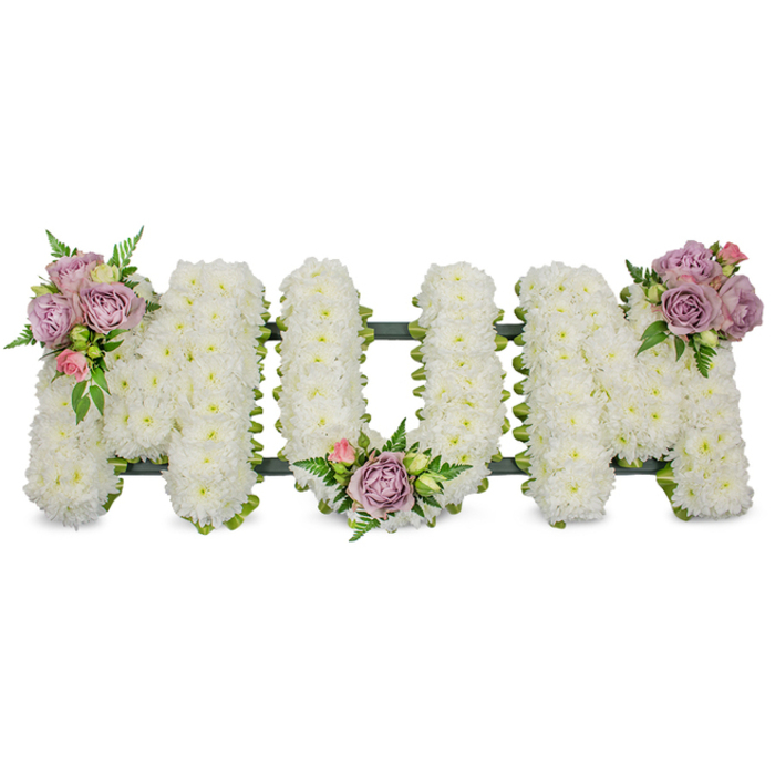 A beautiful and heartfelt memorial artwork spells out the word MUM in clearly defined capital letters, each letter formed from dense clusters of fresh, snow-white chrysanthemums that produce a uniformly soft, textured surface. The white flowers are compacted closely enough to read as a continuous, plush field of petals; in natural or soft studio light they reflect a serene glow that enhances the feeling of peace and quietude. Three small accent arrangements introduce gentle colour: soft lilac roses and pale pink rosebuds are artfully grouped on the upper left curve of the first M, tucked into the inner dip of the U, and placed on the upper right curve of the final M. These pastel blooms, some fully open and others still in tight bud, lend velvety depth and a faint, sweet fragrance that would be noticeable when standing near the tribute. Fresh green foliage-slender fern fronds and lighter green leaves-weaves through and around the blooms, adding contrast and dimensionality while keeping the design organically elegant. A darker green supporting frame, possibly ribbon-wrapped or lined with moss, is visible along the base and subtly outlines each letter, securing the shape and giving the piece a dignified structure. Intended for sympathy and funeral settings across Oxford-from deliveries to chapels around Cornmarket and St Giles to graveside services at local cemeteries-the arrangement communicates loving remembrance and solemn respect. The overall composition is calm, meticulously made and thoughtfully balanced, evoking both the tenderness of memory and the quiet strength of a family's tribute.