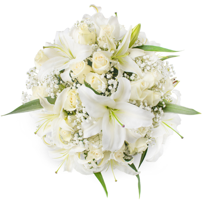 From an overhead perspective, this perfectly rounded bouquet is a refined composition of white lilies, creamy roses and delicate filler blooms, set against a pristine white background that highlights every contour. Prominent white lilies, their wide petals curving outward, reveal pale green stamens and the soft textual contrast of their pollen-bearing filaments; a few show the faintest dusky tones at their centres, adding depth to the otherwise luminous petals. Interwoven among the lilies are numerous cream and ivory roses, presented mostly as tight buds or gently opening cups whose velvety surfaces catch the light in soft gradations. Wisps of Gypsophila (Baby's Breath) weave through the arrangement, creating a lacy, cloud-like veil that cushions the larger flowers and adds intricate detail on closer inspection. Small sprays of vibrant green foliage peek from beneath and around the blooms, framing the circular silhouette and giving the piece a fresh, garden-picked feel. The bouquet exudes a calm dignity and classic beauty - suited to occasions from elegant university weddings by the Botanic Garden to thoughtful anniversary gifts delivered across Summertown or Jericho. Sensory notes are discreet but present: a faint sweet perfume of lilies balanced by the warmer, rounded scent of roses. The deliberate density and symmetry demonstrate the attentive hand of a florist who values both tradition and the quiet modernity of Oxford's streets and ceremonies.