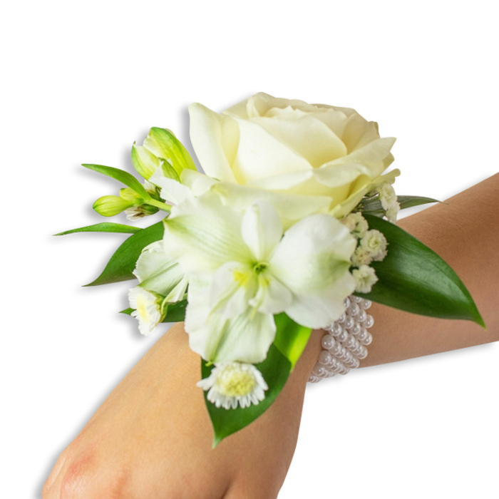 Set against an immaculate white backdrop, this wrist corsage is shown on a light-toned wrist, angled slightly from above so every bloom and leaf is visible. The central focus is a creamy white rose, perfectly formed and softly opening in layers that suggest both youth and timelessness. Just beneath it and a touch to the left, a broad, trumpet-like white flower-recalling an alstroemeria or small lily-displays a gentle lime-green throat that lends the arrangement subtle contrast and an almost botanical intrigue. Interspersed throughout are tiny white gypsophila blossoms, their airy clusters softening the composition, while several fresh green buds-compact and glossy-promise the possibility of further unfolding. At the lower left a small white daisy-style bloom with a sunny yellow centre gives a sweet, playful note against the otherwise classic colour scheme. The flowers are cushioned and framed by deep, glossy green leaves with a smooth, waxy texture that enhances the crisp whites. A slender multi-strand bracelet of uniformly round white pearls secures the corsage: the elastic band allows the pearls to conform neatly to the wrist, creating a tactile contrast of cool, polished beads and warm petals. The overall impression is one of considered craftsmanship-a piece suited to weddings, proms, or formal dances-and evokes images of Oxford mornings near the Isis or quiet moments in Christ Church Meadow. The scent is faintly floral and clean, a whisper of spring that complements the visual serenity rather than overpowering it.