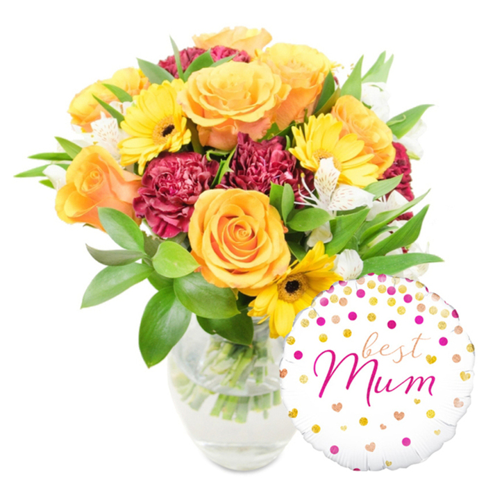 A bright, heartfelt gift set sits against a spotless white background, the bloom cluster centred slightly left while a glossy foil balloon rests to the bottom-right, partially overlapping the vase. The florist's hand is evident in the balance of colours and textures: a group of vivid orange and yellow roses, their petals tightly swirled and satin-smooth, form the focal point and exude a warm, citrus-tinged scent; cheerful yellow gerbera daisies present flat, radiant faces with deep brown centres that catch the eye; and abundant deep-red or burgundy carnations, their ruffled petals compact and velvety, add depth and a luxurious tactile contrast. Fine sprays of white alstroemeria, marked with delicate speckles, weave through the richer tones to add lightness and a whisper of perfume. Lush greenery-broad shiny leaves and slender foliage-frames the flowers, giving fullness and a freshly gathered-from-the-garden feel; the clear glass vase shows the pale green stems and clear water, a small testament to careful preparation. The round white Mylar balloon repeats the celebratory mood: playful gold and fuchsia polka dots and tiny hearts dot its surface, and in the centre a flowing fuchsia cursive proclaims best Mum, the lettering warm and personal. This arrangement, imagined on a kitchen table near Iffley Road or brightening a bedside in Jericho, conveys gratitude and celebration with a refined, homey touch and would be an ideal choice for Mother's Day or a thoughtful birthday surprise around Oxford.