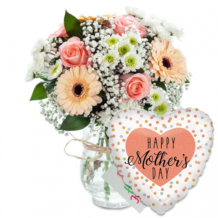 A lovingly arranged Mother's Day gift set is displayed against a clean, uninterrupted white background, allowing the colours and textures to tell the whole story. On the left, a full, rounded bouquet is presented in a clear, jar-style glass vase, the neck wrapped with a simple band of light brown twine that gives the design an unpretentious, homely feel, like something you might proudly place on a dining table overlooking the spires of central Oxford. The bouquet itself is a harmonious blend of springlike tones: soft peach and light pink roses with gently unfurling petals sit at the heart of the design, their romantic curves complemented by striking peach gerbera daisies whose dark brown centres create a strong, cheerful contrast. Floating between these focal flowers, airy clusters of white baby's breath add lightness, while small white chrysanthemums with soft green centres fill in the gaps, giving the arrangement a full and generous profile. Fresh green foliage frames the blooms, peeking out at different heights and angles to lend a natural, garden-fresh appearance, as if the stems had been gathered from a border in an Oxfordshire village garden. To the lower right, partially obscuring the base of the vase, is a large, heart-shaped foil balloon, its crisp white surface scattered with shining gold and silver polka dots that catch imaginary light. In the middle of the balloon sits a solid peach or coral heart, inside which the message HAPPY Mother's DAY appears in elegant black type; HAPPY is rendered in a clean, bold font, while Mother's Day flows beneath in graceful script. Just behind the balloon, a corner of a small white greeting card peeks through, reinforcing the sense of a complete, ready-to-give Mother's Day surprise. This scene evokes the feeling of a thoughtful gift prepared for a mum in Oxford, perhaps waiting on a hallway console before being carried upstairs with breakfast in bed.