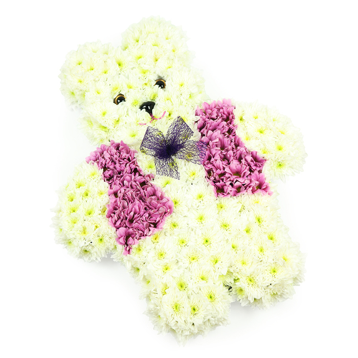 A tender floral teddy bear is shown in full view against a plain white backdrop, its carefully sculpted shape revealing the skill of the florist and the love behind the tribute. Every part of the bear-the softly domed head, petite ears, rounded tummy, and solid, slightly spread paws-is covered in pristine white chrysanthemums. The blooms are placed so closely together that no gaps of foam or foliage show, creating a continuous, plush effect as if the teddy were made from clouds of petals. The chrysanthemums carry a faint hint of cream at their centres, adding depth and a natural warmth to the otherwise snowy colouring. Two small, dark eye details are positioned evenly, and a tiny black triangular nose is nestled between them, giving the teddy a calm, reassuring gaze. A subtle indication of a smile curves beneath, formed by a gentle line in the petals, so the expression remains soft and understated. Across the front of the bear's body sits a floral waistcoat in rich tones of pink and mauve, perhaps echoing the hydrangeas that thrive in many Oxford gardens from Jericho to Marston. These coloured flowers are arranged in two side panels, leaving a slim central space for a delicate bow of purple net, tied at the neckline. The bow's translucent layers add a touch of lightness and movement to the design. Illuminated by clear, even light, the arrangement feels pure and serene. This floral teddy bear would sit beautifully by a small coffin in an Oxford chapel or at a crematorium service, offering a gentle symbol of love, remembrance, and cherished childhood.