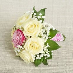 Envision a hand-tied bouquet carefully resting on a creamy beige linen, the kind of natural woven fabric found in quintessential Oxford boutiques. The design speaks in poetic tones-five rich, cream-hued roses, their petals opening in serene spirals, set the foundation for a refined celebration. Nestled warmly within them, a single fuchsia-pink rose glimmers vibrantly, its lively color echoing the creative energy of Oxford's High Street in bloom. Wispy branches of baby's breath float throughout the florals, weaving brightness and a weightless charm, much like early morning fog drifting over Magdalen College gardens. Lush, dark green leaves, polished and firm, cradle the flowers and provide grounding, contrasting the bouquet's softness with reassuring clarity. The handle, wrapped seamlessly with bright pink satin and finished in a spiral of tiny, luminescent pearls, offers a contemporary nod, reminiscent of Oxford's harmonious blend of tradition and trend. Illuminated by diffused, gentle light, each element stands out in nuanced detail-the gentle curve of petals, the freshness of greenery, the crisp woven texture beneath. Freshness and artistry combine, channeling the essence of events along the Thames or within ancient halls, making this bouquet an ideal companion for an Oxford wedding or a tender moment of celebration.