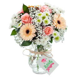 Transport yourself to a crisp Oxford morning with this enchanting bouquet-a masterful blend of soft peach and blush-pink roses unfolding at the centre, flanked by vivacious peach-orange gerbera daisies. The arrangement is alive with contrasts: velvety petals radiate gentle romance, while the daisies' bold simplicity adds an inviting hint of joy, much like the lively air along High Street as the city awakens. Among these, clouds of delicate white baby's breath impart an airy, innocence, drifting softly between the larger flowers. Clusters of round, white chrysanthemums with fresh green centers evoke the freshness of the Botanic Gardens after rain, adding subtle depth without overpowering the bouquet's pastel theme. Carefully chosen leaves, likely silvered eucalyptus or viburnum, are tucked in with deliberate ease, their scent faint yet invigorating. A clear, textured glass vase cradles the bouquet, the intertwining stems visible and reassuringly natural, topped with a knot of rustic raffia or twine. Attached, a simple white tag awaits your personal inscription, set to turn this elegant bouquet into a bespoke gift. Bright, even lighting dances across the arrangement, enhancing every nuance of colour and texture. Whether meant for a college milestone, a celebration on Magdalen Bridge, or an intimate gathering at a Summertown café, this bouquet radiates tranquility and understated Oxfordian charm-a tender tribute from a local florist deeply in tune with the city's rhythms.