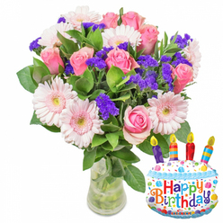 In soft, directional light that highlights texture and colour, this birthday bouquet presents a harmonious blend of romance and festive cheer. At its heart are numerous soft pink roses, their petals layered and slightly cupped, moving from pale blush centers to warmer pink edges-a tactile, velvety look that invites a breath of their gentle scent. Scattered among them are large, pale-pink Gerbera daisies whose open, circular faces and subtle yellow centers lend a playful, almost smile-like energy to the arrangement. Bringing lively contrast and sculptural texture are clusters of vivid purple statice or limonium, their crisp, papery flowers threaded through the bouquet to create depth and multi-dimensional interest. Small white filler blooms, perhaps spray carnations or alstroemeria, nestle in the mid-foreground, softening transitions between the larger flowers. Glossy green foliage frames the bouquet, leaves of varying sizes and surfaces that ground the composition and suggest a freshly gathered feeling. The flowers are anchored in a clear glass vase with a slightly wider base, stems visible and neatly trimmed in clear water-an honest, unfussy presentation that emphasizes freshness. To the right, a cheerful foil balloon shaped like a layered birthday cake adds a celebratory note: white frosting details, blue piping, and scattered multicolored sprinkles, topped with four striped candles and multi-coloured "Happy Birthday" lettering. A small 'KALEIDOSCOPE' brand mark appears at the bottom of the balloon. As composed by a florist who knows Oxford's tastes-from the Covered Market to Jericho-this arrangement balances classic floral elegance with a lighthearted accent that feels right for birthday table centres or a thoughtful doorstep surprise.