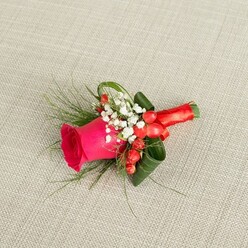 This image shows a carefully crafted buttonhole resting on a pale beige, slightly textured fabric that looks like finely woven linen, the sort you might find in an elegant Oxford townhouse off Banbury Road. At the centre of the arrangement, a hot pink rose glows with saturated colour, its petals layered tightly at the core and gradually opening into a soft, velvety spiral that speaks of fresh, early-morning work at the florist's bench. Enveloping the rose is a collar of deep green foliage, some leaves folded and curled with architectural precision to hold the flower proudly upright, while airier, fern-like fronds spill outward to add movement and a sense of gentle coolness. Tucked between the greenery, tiny white flowers of baby's breath form a lacy halo, their miniature blossoms giving the design a feeling of innocence and tradition often chosen for church weddings around Jericho and Summertown. Near the base of the rose, clusters of small, round, scarlet hypericum berries provide a rich, glossy accent, as if dots of warm light have been brushed onto the arrangement. The stems are wrapped smoothly in a bright red satin ribbon, folded and secured so the underside will sit comfortably against a jacket lapel, whether worn at a registry office near St Aldate's or a college hall reception. The natural daylight falls gently across the scene, creating soft shadows that highlight the textures of petal, leaf, and fabric. Overall, the buttonhole radiates heartfelt celebration and quiet sophistication, a tiny floral sculpture that captures the joy and anticipation of a special day in Oxford.