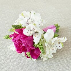 A small, carefully composed bouquet rests sideways on a pale beige, linen-like cloth, its subtle texture serving as a calm canvas for the intense colour of the flowers. Dominating the centre is a fully open magenta peony, its petals densely layered in soft, frilled folds that seem to spill outward in a generous, almost cloud-like shape. Surrounding this bold focal bloom, pure white alstroemeria flowers unfurl with quiet grace, each trumpet-shaped blossom displaying six fine petals etched with burgundy and maroon streaks that fan out from the throat, adding the sense of handwritten notes across the petals. Threaded through the composition are slim, upright sprays of vivid green buds and spiky florets, giving a fresh, garden-picked feel and introducing a linear texture that balances the abundance of ruffles. The green stems are gathered tightly together and wrapped in a bright fuchsia satin ribbon whose sheen catches the light, echoing the peony's rich tones and hinting at the care taken by the florist in tying the final knot. The light falls gently over the flowers, revealing subtle shadows at the base of each petal and a soft glow along the edges, as though the arrangement has just been placed down between photos on a wedding morning in Oxford, perhaps in a townhouse near Summertown or a boutique hotel by the High Street. There is a sense of intimate celebration, as if this could be a bridesmaid's posy, a groom's statement boutonnière, or a special corsage prepared for a formal dinner, capturing the joyous, romantic energy of a spring ceremony in the city's historic streets.