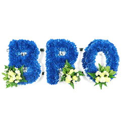 A reverent, three-piece memorial spelled BRO, photographed on a clean white studio backdrop so every detail reads clearly. Each capital letter-B, R and O-is formed from thousands of small royal blue chrysanthemum heads packed tightly to create a lush, textured surface reminiscent of deep summer velour. The B at left shows two rounded lobes, the R in the centre balances solidity with a delicate tail, and the O is a flawless ring; all edges are sharply defined against the white foam frame that supports the blooms. At the lower left of the B and the lower right of the R and O, we've placed tasteful accent clusters of pale yellow-to-ivory spray roses, mingled with tiny white filler chrysanthemums or baby's-breath-like blooms and mixed greenery-broad shiny leaves for weight and softer ferny fronds for movement. The arrangement is gently lit to reveal the tactile quality of the chrysanthemums and the satin softness of the roses; a faint fragrance of rose and fresh green foliage seems almost perceptible. Set by an experienced Oxford florist, this design quietly communicates loyalty and remembrance-royal blue traditionally suggesting peace and sincerity-making it a solemn, personal tribute for a brother or close friend at a funeral, memorial or chapel service in areas like Jericho, Summertown or near the Botanic Garden.
