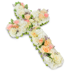 A beautifully composed floral cross, reminiscent of the thoughtful tributes often seen in Oxford's old stone churches, fills the centre of the image against a clean, brilliant white background. The entire Christian cross is constructed from tightly massed flowers, so that every inch is covered in soft petals, creating a thick, cushioned appearance. The colour palette is gentle and comforting: white and ivory form the foundation, while soft peach, apricot, and blush-pink roses bring warmth and subtle colour. Larger roses, some fully open and others delicately budding, are placed in small clusters across the cross, drawing the eye naturally from top to base and along each arm, almost like a quiet pathway of memories. Between these focal blooms, mounded clusters of fluffy white hydrangea, along with smaller white spray roses or similar blooms, fill the gaps and add a sense of abundance. Their rounded, cloud-like texture helps soften the outline so the cross appears lovingly hand-shaped rather than rigid. Tiny hints of lavender-coloured filler flowers are scattered with restraint, providing little sparks of pale purple that give extra detail when viewed closely. Peeking from beneath the flowers, discreet touches of fresh greenery trace the contours and add definition, ensuring the cross shape remains clear and harmonious. The soft, even lighting picks up the creamy undertones in the ivory petals and creates a light shadow below, giving the design dimension without distraction. Intended as a funeral or memorial arrangement, this floral cross conveys peace, faith, and heartfelt condolence, offering a dignified way for families in Oxford to honour a loved one with a symbol of hope and enduring love.