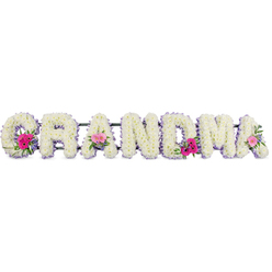 The image shows a carefully crafted funeral flower tribute spelling "GRANDMA," the letters arranged in a graceful row as if gently resting in stillness. Every character is built on a sturdy frame then completely blanketed with snowy white chrysanthemums, their cushiony petals overlapping to form a soft, velvety texture. The blooms are fresh and full, suggesting that they were prepared the same day for a service somewhere in Oxford, perhaps near Headington or Summertown. A neat border of lilac ribbon runs around each letter, the satin edge catching the light and adding a refined, pastel halo that softens the strong shapes. Three focal points of colour draw the eye: dainty posies placed on the starting G, a central A, and the closing A. These miniature bouquets combine bright pink gerberas with their neat, daisy-like petals, smaller pink roses at different stages of opening, and sprigs of rich green foliage that curl and fan outward, bringing a touch of garden freshness. The greens echo the calm of college quadrangles and leafy streets off the Cowley Road, while the pinks bring a quiet sense of joy and gratitude. The overall lighting is gentle and diffused, allowing every curve of petal and fold of ribbon to be clearly defined without harsh shadows. You can almost imagine the soft rustle of stems being placed, the subtle fragrance of chrysanthemum and rose, and the hushed atmosphere of a farewell gathering. This floral lettering feels both strong and tender, a loving tribute arranged by an experienced local florist who understands the importance of honouring a grandmother with grace and beauty.