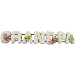 The image shows a dignified floral memorial spelling GRANDPA in large, three-dimensional letters, arranged in a single line as if ready to rest beside a coffin at an Oxford crematorium or church. Each letter is built entirely from tightly clustered white chrysanthemums, the petals forming a plush, almost cloud-like texture that suggests purity, peace, and the comfort of shared memories. A fine edging of pale lilac or lavender ribbon folds neatly around the base of each letter, giving subtle definition and a gentle wash of colour that softens the strong block shapes. The letters sit along a dark green frame, mostly hidden behind the blooms, giving the tribute the strength to be carried to a graveside in Oxford's quiet cemeteries or laid respectfully by the chapel doors. Colourful sprays interrupt the white in carefully balanced intervals. On the 'G' and the 'D', rich red anthuriums with waxy, heart-shaped faces and creamy-yellow spadices nestle among lush green foliage, radiating love, respect, and gratitude for a grandfather's life. On the first and final 'A', clusters of yellow-green orchids arc gracefully over the chrysanthemums, their exotic petals and buds offering a sense of hope and enduring beauty. Smaller leaves and filler greens thread through the accents, adding depth and a natural garden feel. The overall impression is one of solemn tenderness: a bespoke funeral tribute designed to say Grandpa in flowers when words feel insufficient, perfectly suited to a farewell service anywhere across Oxford, from local parish churches to crematoria chapels by the ring road.