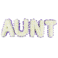 This photograph shows a lovingly arranged tribute spelling A U N T, each bold letter lovingly filled with hundreds of small white spray chrysanthemums that form a plush, textured surface. The tiny florets create a soft, almost cloudlike appearance, while occasional pale yellow disc centres add a reassuring touch of natural colour and detail. Around the edge of each letter a deep purple satin ribbon has been carefully pleated and fastened, the ribbon's sheen offering a refined contrast against the matte white of the blooms and tracing every curve and angle of the letter frames. Low, cool shadows beneath the letters emphasise their sculptural presence on the white background, suggesting a solid, framed construction that will hold up at a chapel or graveside service. As an experienced florist serving areas from Summertown to Cowley, I note the balance here between dignity and warmth: the white chrysanthemums speak of respect and memory, while the purple ribbon lends a thoughtful, almost celebratory nod to a life well-loved. The scent is soft and green, a delicate freshness that supports rather than competes with the moment. This arrangement is composed for clarity and comfort, suitable for laying beside a photograph at a service or for display in a church or crematorium room in Oxford. Finished with neat wiring and a satin edge, it's a bespoke expression of affection and farewell, crafted with the kind of care local families expect.