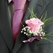 There's something quietly poetic about this Oxford-crafted buttonhole, a floral arrangement that captures the promise and romance so often found amidst the city's historic venues. Central to the design is a blush-pink rose, its soft, velvet petals unfurling gracefully, subtly illuminated as if by gentle morning light streaming through a college window. Around the rose swirl delicate sprays of baby's breath, their snowy, miniature blossoms creating a feathery surround that accents the central bloom's charm. Wispy green foliage arches behind, contributing refreshing energy and balance-suggestive of the serene paths lining the Cherwell. The ensemble is finished with a lustrous satin ribbon in lilac, providing a final touch of sophistication. The boutonniere stands out against a deep grey suit, complemented by a vivid, fuchsia-pink tie and a subtly patterned shirt, all chosen with thoughtful precision. For celebrations from Bodleian banquets to riverside weddings in Oxford, this creation is more than floral artistry-it's a sensory token of joy, anticipation, and the lasting bonds Oxford has inspired for generations.