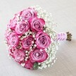 Resting atop finely woven linen in a softly lit Oxford studio, this round bouquet immediately draws the eye with its lively array of ten to twelve double-toned roses. Their centers glow with dusty lavender-pink, crescendoing outwards to deep magenta and fuchsia-a color play reminiscent of Oxford's vibrant floral corners along the Cherwell in spring. Embroidered between each rose, the pure white baby's breath embraces the arrangement with a misty, cloud-like texture, lending airiness and poetic grace. The hand-tied stems are wrapped with care in a radiant blush satin ribbon, their ends neatly trimmed but left charmingly natural, while a dainty curl of white pearls adds just the right hint of sophistication for a Carfax wedding or intimate celebration in North Oxford. The bouquet's elegant, dome-shaped profile is crafted for comfort and visual impact, and the lighting captures every velvety petal and glimmering pearl, amplifying the bouquet's fresh, heartfelt energy. This design evokes images of happy couples under dreaming spires, of family gatherings near University Parks, and celebrations where love, beauty, and tradition meet. Each detail-from the harmonious color gradation to the soft interplay of textures-tells a story only an experienced Oxford florist can narrate, making it the ideal arrangement for marking life's most meaningful milestones.