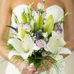 A refined bridal bouquet that captures the hush and hope of wedding mornings in central Oxford, this arrangement centers on lofty, alabaster lilies whose open faces radiate a soft, pearl-like light. Around them, purple-tinged lisianthus provide elegant punctuation-their gently scalloped edges and cool mauve halo lending depth and a modern romanticism to the composition. Small veronica spikes and tight buds peek between larger blooms, introducing subtle vertical rhythm, while cushions of baby's breath scatter like tiny, luminous constellations across the design. Wisps of fine green grass and trailing filigree foliage add a delicate sense of motion, framing the blooms so they appear poised yet effortless in the hand. The bouquet's scent is gently intoxicating: classic lily sweetness balanced by fresh, green notes that evoke early-morning air in University Parks or a riverside stroll by Folly Bridge. Careful layering ensures each stem reads clearly in the soft daylight, giving the bouquet a gracious architecture that suits both a formal chapel service and an intimate garden fête near the Covered Market. Skillfully assembled by Flowers Oxford florists with a sensitivity to texture, light, and scale, this bouquet feels personal and timeless-an expression of devotion presented with subtle luxury and floristry finesse, meant to accompany the bride through vows and photographs across Oxford's historic streets and green spaces.