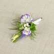 A finely detailed wedding boutonniere lies against a softly textured light beige linen cloth, the neutral background allowing every petal and ribbon to stand out with quiet clarity. At its heart are two open lisianthus blooms, their petals a luminous white with deeply ruffled edges traced in rich purple, creating a gentle halo of colour that feels both modern and timeless. Clustered around them are tiny white filler flowers, like a cloud of baby's breath, that soften the design and add an airy, almost whisper-light texture. A slim vertical spike of tightly packed, deep purple muscari buds rises through the centre, their bell-shaped flowers echoing the tones at the lisianthus edges and lending depth and structure. Two pale green buds, still closed, peek from the side, suggesting freshness and the sense of a day just beginning-perfect for a ceremony morning in Oxford, perhaps near the historic colleges or along the High Street. Fine, feathery greenery, reminiscent of asparagus fern, fans out delicately beneath the blooms, its soft fronds framing the flowers like a natural collar and adding movement to the composition. All the stems are neatly gathered and wrapped in crisp white satin ribbon, finished with a small, careful bow that signals it is ready to be pinned on a lapel with pride. The light in the image feels gentle and natural, highlighting the clean whites, cool purples, and fresh greens, and capturing the calm anticipation of a wedding or prom. It's the kind of thoughtful buttonhole a seasoned Oxford florist might create for a groom or groomsman who wants refined elegance without excess.