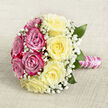 Captured from a softly elevated angle, this classic, hand-tied rose bouquet lies on a pale, textured fabric that looks like fine linen in warm beige, giving the scene a calm, timeless backdrop. The arrangement is perfectly rounded, almost like a pastel sunset divided in two: one half is filled with vibrant magenta-pink roses, lush and velvety, each bloom open to reveal intricate spirals of petals; the other half showcases smooth, buttery yellow roses, their creamy tone gently diffusing into softer edges as the petals unfold. Scattered delicately throughout both sides, airy sprigs of white gypsophila form a light, cloud-like veil, softening the boldness of the roses and adding that traditional bridal touch so often requested for Oxford town-hall weddings or ceremonies in Summertown churches. Slim, glossy green leaves occasionally peek through, lending structure and a whisper of garden freshness, as if the flowers were just gathered from a well-kept border in Headington or a cottage garden near Iffley. The stems are firmly bound in a tight, expert grip, wrapped in lustrous pink satin ribbon that lies smooth against the hand. Around this, a string of delicate white pearls coils in a gentle spiral, providing texture and a subtle glimmer reminiscent of heirloom jewellery. The overall effect is elegantly romantic and slightly nostalgic, suitable for a bride crossing one of Oxford's historic quads, for an anniversary dinner overlooking the dreaming spires, or as a refined romantic gesture. The bouquet's visual balance between warm yellow, confident pink, and soft white suggests affection, joy, and lasting commitment.