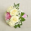 Resting gently atop light beige linen reminiscent of Oxford's classic interiors, this compact bouquet shines with the quiet elegance beloved in the city's historic venues. The arrangement features five creamy white roses, each bloom delicately unfurled to reveal intricate layers and a sense of plush fullness. A single, brilliant magenta rose lies just off-center, offering a joyful burst of color-much like the vibrant displays found at Oxford's Botanic Garden in midsummer. Wisps of white gypsophila thread through the roses, lending an airy, celebratory tone and softening each edge with a whisper of tradition. Deep green leaves frame the floral arrangement, adding depth and contrast for visual harmony. Bound at the base, a bright fuchsia-pink ribbon wraps the stems tightly, further adorned by a spiral of luminous pearls, imbuing the bouquet with a sophisticated sparkle. Illuminated by mellow, natural light that highlights the freshness of each petal and the smoothness of the ribbon, the bouquet evokes a timeless sense of romance and ceremonial joy-perfect for bridal parties, intimate gatherings, or heartwarming celebrations across Oxford's beloved colleges and event spaces.