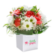 A radiant bouquet overflowing with the spirit of Oxford springs forth from a sleek white gift bag-its colours and textures the very picture of seasonal abundance and joy. Soft, coral-tinted carnations with exuberantly ruffled petals mingle with vibrant ruby-red blooms, creating an inviting contrast that catches the light, much like wildflowers basking on Port Meadow. Dazzling white daisies, each crowned with a joyful yellow-green center, nestle among the richer hues, offering a bright, uplifting accent. Between them, baby's breath drifts in fluff-like clouds, imparting a softness that feels almost weightless to the eye and heart. A subtle sprinkling of closed buds tinged with purple peeks from the arrangement's edge, hinting at the promise of unfolding beauty yet to come, like the blossoming of spring along Cowley Road. Generous swathes of gleaming dark green leaves embrace the bouquet, weaving all the elements together in a harmonious embrace. The arrangement stands proudly in its minimalist white bag, whose clean lines and strong handles speak of convenience as well as style-a gesture perfected for a birthday surprise in North Oxford or a heartfelt thank-you delivered across Headington. Bathed in gentle, natural light, this bouquet radiates freshness, care, and the joyful spirit of giving so valued in the Oxford community.