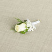 Deliberately simple and refined, this boutonniere centers on an immaculate ivory rosebud whose velvety layers are pressed into a graceful, compact spiral. Encircling the bloom, tiny white gypsophila blossoms create a soft halo, lending a breath-like lightness that offsets the deeper, verdant tones of accompanying foliage. Slender, almost feathery sprigs of dark green-suggestive of cedar or an evergreen accent-add a textured verticality, while broader deep-green leaves offer structural balance and frame the flower with a rich backdrop. The stems are bound with a satin-white ribbon, smoothed and tied into a small, precise bow, the satin catchlight mirroring the fabric sheen beneath. Set diagonally on a natural, woven beige cloth, the arrangement sits in gentle daylight, which reveals the fine veining on the petals and the subtle contrast between matte leaf surfaces and glossy ribbon. There is a delicate, almost powdery scent that accompanies the rose, a fragrance that brings to mind early-morning walks through University Parks or the hush of an Oxford cloister at dawn. As a piece of wearable floristry, it reads as both ceremonial and intimate-appropriate for a father of the bride walking down a High Street of small gathering venues, or for a best man fastening a finishing touch before photos by the Radcliffe Camera. The overall impression is one of considered restraint: fresh, handcrafted, and quietly celebratory, a small emblem of purity and new beginnings held close to the heart.