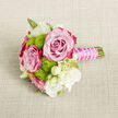 On a softly textured, light beige fabric that resembles natural linen, a petite yet luxurious bouquet lies gently as if waiting to be lifted for a special moment in Oxford. The neutral background enhances every nuance of colour: two large roses sit at the centre, their petals unfolding in flawless spirals. The inner petals are a tender, almost translucent blush, gradually deepening to a rich fuchsia or magenta around the edges, like a sunset over the dreaming spires. Their condition is immaculate, with no bruising or blemishes, conveying the care of an experienced florist. Tucked closely around the roses are clusters of lime-green button chrysanthemums, each tiny bloom tightly packed and perfectly round, contributing a lively, tactile texture. Their vivid green contrasts beautifully with the pinks, echoing the fresh greens of Christ Church Meadow in spring. Scattered among them are fine white flowers and buds, perhaps lisianthus or freesia, their ivory petals slim and graceful, some open to reveal soft yellow-green centres, others still curled in creamy anticipation. A few narrow green stems and leaves weave through the composition, adding natural rhythm and shape. The stems are cut short and bound into a compact handle, wrapped smoothly in a fuchsia satin ribbon that mirrors the deeper tones of the roses. Over this ribbon, a strand of small white pearl-like beads is wound in a gentle spiral, giving the handle an elegant, almost jewellery-like finish. The overall impression is of a perfectly considered mini-bouquet, ideal as a boutonnière, corsage, or small bridesmaid cluster for an intimate celebration or registry wedding near Oxford's historic town hall, radiating quiet romance and festive charm.