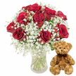 The photograph presents a romantic gift set arranged as if it were ready to be delivered to a loved one in Oxford, the whole scene framed by an immaculate white background that highlights every texture and colour. On the left, a clear, straight-sided glass vase holds a sumptuous bouquet of about twelve deep red roses. Each rose is rich with velvety petals, layered tightly towards the centre and loosening at the edges into soft, full blooms. Some flowers appear freshly opened, others slightly more mature, giving the arrangement an organic, garden-fresh look you might associate with a florist tucked near Oxford's covered market. Delicate sprays of white baby's breath drift through the roses, their countless miniature blossoms creating a fine, cloud-like haze that gently softens the vivid crimson. The play of red, white, and flecks of dark green foliage creates an elegant contrast, suggesting both passion and tenderness. Through the transparent vase, straight green stems are visible, partially submerged in clear water that catches the light in a subtle gleam. To the right of the bouquet, a plush teddy bear sits poised and upright. Its light brown fur looks cushioning and soft, as if it would be warm in your hands on a cold evening after a walk by the Bodleian. The bear's small black button eyes, rounded ears, and neatly embroidered nose combine to form a gentle, friendly gaze. A slim, dark brown ribbon is tied snugly around its neck in a simple bow, echoing the classic style of the roses. Altogether, the image evokes feelings of affection and heartfelt connection-a scene perfectly suited to illustrate flower and teddy delivery across Oxford for anniversaries, romantic surprises, apologies, or birthdays, from Jericho to Headington.
