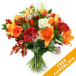 A hand-tied, autumnal bouquet arranged upright against a pristine white backdrop, the composition glowing with warm oranges, deep reds and russet tones. At the heart of the arrangement several large, open orange lilies present broad trumpet-shaped petals and prominent stamens, while a few unopened lily buds promise a later, gentle unfurling. Scattered among them are cheerful Gerbera daisies in shades from ruby red to bright pumpkin orange, their concentric petals forming lively, sunburst centers. Creamy-white Lisianthus with ruffled, satiny petals offer cool contrast and a soft, delicate texture. Small, star-like Astrantia with purple-pink centres and lacy bracts add an intricate, almost woodland detail that draws the eye into the bouquet's depth. A cushion of glossy deep green foliage - likely ruscus or salal - provides a verdant base and frames the blooms, while several large, deeply lobed oak leaves in burnt orange and reddish-brown are woven through the stems to reinforce the season's palette and add structural silhouette. The stems are neatly gathered and tied low with dark twine or raffia in the classic hand-tied style, leaving the natural stems visible and fresh. The whole piece sits in soft, even studio light that highlights petal textures and the subtle sheen of leaves, evoking the crisp calm of an Oxford autumn walk near the Botanic Garden. In the lower right corner an orange diagonal banner overlays the image, clearly stating the words FREE CHOCOLATE in bold white letters - a visual callout on the image rather than part of the flowers themselves. The bouquet's tone is warm and celebratory, perfect for a seasonal gift or delivery within the city.