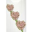 Three delicately crafted heart-shaped tributes form a vertical column, each heart appearing to float one beneath the other against a clean, bright white background. Their outlines are created from slender, intertwining green vines and sprigs of ivy, the foliage looping gracefully around each curve and adding a fresh, natural frame. Within these leafy borders, tightly clustered small roses cover the entire surface of each heart, giving a lush, velvety appearance that feels soft even from a distance. The colour palette is gentle and romantic: muted dusty pinks, soft mauves and hints of lavender blend together, with occasional lighter petals catching the light like tiny shells. The top heart leans slightly to the left, while the two below step gradually to the right, all connected by thin strands of greenery that run between them, suggesting a continuous thread of love and memory. The seamless white backdrop is reminiscent of a bright studio space or a modern chapel near Oxford's Jericho or Iffley Road, where the focus remains firmly on the flowers themselves. You can almost imagine the faint, sweet fragrance of the roses, calm and comforting rather than strong. This elegant composition would feel at home at a funeral or remembrance service in Oxford, perhaps displayed near a book of condolences or at the front of a quiet church. The three hearts speak of shared lives and intertwined stories, their handcrafted detail reflecting the care and respect that goes into creating a meaningful farewell tribute for someone treasured.