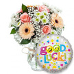 A bright, encouraging 'Good Luck' gift ensemble set against a clean white backdrop: to the left sits a generous, loosely gathered bouquet in a clear glass vase tied with a simple twine bow, the kind of artisanal finishing touch a neighbourhood florist would add. The arrangement mixes soft peach and light pink roses with warm peachy-orange Gerbera daisies whose dark brown centers give a pleasant, grounding contrast. Wisps of delicate white baby's breath (Gypsophila) drift through the blooms like lace, while tight clusters of small white and lime-green chrysanthemum-style florets add a crisp, vivacious texture. Deep green foliage peeks between petals, giving depth and a natural silhouette to the stems. The glass shows the cut stems faintly below, catching soft, neutral studio light that emphasizes the petals' satiny textures.In the right foreground, partially overlapping the vase, a round silver metallic foil balloon takes centre stage: its shimmering silver surface is scattered with tiny colourful shapes - blue and pink hearts, yellow and blue stars, and little orange and green cross-like motifs - sending a playful confetti effect across the composition. The bold message Good Luck! arches across the balloon in a bubbly, multi-coloured font; the letters are lively greens, oranges, reds and blues and one of the playful yellow smiley faces is integrated into the lettering, winking or sticking out its tongue depending on the viewing angle. A small KALEIDOSCOPE logo sits at the balloon's lower edge.The overall mood is hopeful and celebratory, evoking gentle fragrance from roses and the crispness of chrysanthemums. This is an ideal gift for exams, interviews, farewells or new beginnings - a thoughtful bouquet a local Oxford florist might deliver to friends studying at the University or celebrating milestones near the Covered Market or High Street.