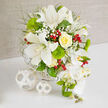 An opulent, contemporary bouquet in shades of white, green, and gentle yellow is displayed on a clean white table, set against a softly textured beige wall that could belong to a refined Oxford venue near Jericho or Summertown. The main blooms are tall, star-shaped Oriental lilies, their pure white petals fully unfurled and dusted with faint speckles, with bold stamens adding a warm accent at their centers. Tucked closely beside them, a single yellow rose, perfectly cupped and creamy at the edges, becomes a quiet focal point that radiates warmth and understated joy. Throughout the design, fine clouds of white baby's breath spill between the larger flowers, softening the transitions and creating a dreamy, veil-like effect that feels particularly suited to a bridal table. Striking tufts of bright green dianthus and other verdant elements add structure and a playful, moss-like texture, while feathery foliage stretches outward, giving the bouquet movement and depth. Small clusters of polished red hypericum berries punctuate the soothing palette, like festive notes scattered through a classical melody. On the right, a flowing trail of white Phalaenopsis orchid blooms slips gently over the edge of the arrangement, each orchid petal smooth and satin-like, with hints of yellow at the throat and a few firm green buds promising more flowers to come. The entire composition is anchored in a white woven basket, accompanied by two matching wicker spheres on the left side of the table, reinforcing the modern, curated feel. It's a centerpiece that would sit beautifully at an Oxford wedding breakfast, perhaps overlooking the river near Folly Bridge or a reception in one of the historic colleges.