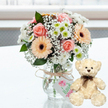 On a clean, white, lightly reflective tabletop, a charming anniversary gift duo is arranged with the care of a local Oxford florist. At the centre, a rounded, compact bouquet sits in a clear glass jar, its stems visible through the water like green brushstrokes. The flowers themselves are soft and romantic: pale pink roses, peach or apricot gerbera daisies with distinct dark brown centres, bright white chrysanthemums touched with a hint of lime at the core, and delicate clouds of white baby's breath filling the spaces in between. This gentle mix of pastels and crisp whites feels like a stroll through University Parks in early spring. Around the vase's neck, rustic natural twine is tied into a simple bow, supporting a light-toned gift tag illustrated with a small pink motif and faint green lettering that hints at a handcrafted, personalised touch. To the right, a small, cream-coloured teddy bear sits upright, angled very slightly toward the flowers as if sharing in the celebration. Its plush fur appears soft and cuddly, with dark bead eyes, a brown stitched nose, and a dark brown satin ribbon tied neatly around its neck, all adding to its comforting presence. The softly blurred background suggests a sunlit window in an Oxford home, allowing the bouquet and bear to stand out clearly. The overall impression is one of warmth, tenderness, and quiet joy, ideal for marking an anniversary, a first date remembered, or any loving milestone celebrated across Oxford, from the historic colleges to modern apartments in Headington and beyond.