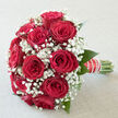 A luxurious bouquet of red roses and snowy gypsophila appears in calm, diffused daylight, as if resting on a dressing table in an Oxford townhouse before the wedding party departs for the ceremony. The roses are a rich, velvety crimson, each bloom cupped in a classic spiral that speaks of enduring romance and carefully considered craftsmanship. Nestled between them, sprays of white baby's breath create a fine, cloud-like texture, each minuscule flower adding softness and a hint of innocence, like early morning mist along the Thames Path. The florist has shaped the bouquet into a rounded, harmonious dome, with foliage tucked discreetly underneath so the focus remains on the interplay between bold red and luminous white. The stems are gathered tightly and wrapped in satin ribbon, accented with a line of small pearls that catch the light with understated grace, echoing the refined charm of Oxford colleges and chapels. You can almost feel the contrast beneath the fingertips: the firmness of the stems, the plushness of the rose petals, the feather-light touch of the gypsophila. A subtle rose fragrance seems to hover in the air, soft yet unmistakably romantic. This arrangement looks perfectly at home in wedding photographs taken in Radcliffe Square or outside a historic registry office, but it would be equally fitting for an anniversary dinner in Jericho or a surprise delivery to a loved one overlooking the dreaming spires. The entire scene communicates devotion, celebration, and that quiet, timeless elegance Oxford is known for.