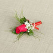A petite yet striking boutonnière showcases a vivid magenta-pink rose, its tightly layered petals forming a soft, velvety cup that draws the eye immediately. Around it, deep green foliage and slender, arching grass blades create a gentle halo, the fine lines of greenery adding texture and a feeling of light, effortless movement. Nestled beside the central rose are airy tufts of white baby's breath, each tiny bloom like a pearl of light against the richer tones, giving the arrangement a romantic, almost vintage charm that would suit a ceremony in one of Oxford's historic chapels or college halls. The stem is expertly finished with a bright red ribbon, coiled neatly and smoothly from top to bottom, catching the light with a subtle sheen; its bold colour suggests celebration, warmth, and the excitement of a wedding day or graduation gathering on Broad Street. The boutonnière lies against a neutral, lightly textured background, reminiscent of a tailored suit laid out in a quiet room before the festivities begin. As a florist working in and around Oxford, I recognise in this design the quiet confidence that many couples seek: a single rose that carries emotion without excess, elegant enough for a groom, best man, or prom guest. You can almost sense the faint, sweet fragrance rising from the bloom, mingling with polished shoes and crisp linen. Every curve of greenery, every cluster of gypsophila, and each turn of ribbon reflects experienced hands and thoughtful design, ready to be worn close to the heart during life's most cherished celebrations.