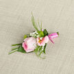 This boutonniere is composed like a careful love letter, with a full, blushing pink rose at its centre, opening in neat spirals of soft petals that glow gently in the light. The rose is surrounded by pastel alstroemeria blooms, their pale pink petals brushed with soft stripes and warm yellow throats, echoing the delicate colours of spring blossoms along Oxford's parks and college gardens. Threaded between them, tiny white gypsophila blossoms create a constellation of fine points, giving a cloud-like softness that contrasts beautifully with the structured rose. Fine green fronds and small, curled leaves add texture and freshness, each stem placed with a florist's precision so the arrangement feels balanced and effortless. The stems are bound in a smooth, satin-like pink ribbon, tightly wrapped and neatly finished, as immaculate as a tailored suit worn for a wedding at an Oxfordshire manor or a celebration near the Botanic Garden. Resting on textured fabric, the boutonniere appears ready to be pinned to a lapel, its colours standing out gently yet confidently. You can almost feel the velvety touch of the rose, the feathery lightness of the baby's breath, and the crisp edges of the foliage between your fingertips, with a soft, fresh fragrance that suggests an early-morning delivery across Oxford. This design would suit a groom, usher, or special guest, lending a quiet grace that reflects both personal sentiment and thoughtful local craftsmanship.
