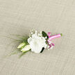 A delicate white lisianthus boutonniere lies gently on a neutral, woven fabric, the sort of natural texture you might find on a linen table in an Oxford High Street townhouse. The main bloom is a fully opened lisianthus flower, its creamy white petals layered in soft, ruffled spirals that radiate from the centre, creating an impression of depth and quiet abundance. Two smaller lisianthus buds lean in towards the larger flower, their smooth, tapered shapes still closed, suggesting new beginnings and tender expectation. Interspersed among them are dainty sprigs of baby's breath, each stem branching into clusters of tiny white blossoms that lend a misty, ethereal quality, like light morning fog drifting over Christ Church Meadow. Slender green leaves and reedy stems provide a refreshing contrast, their fine lines and subtle curves introducing rhythm and movement to this petite arrangement. All the stems are meticulously bound together in a bright pink satin ribbon that gleams softly under the light. The ribbon is wrapped smoothly and finished with a tidy bow, its bold colour adding a cheerful, modern twist to the classic white-and-green palette. The overall impression is one of intimate elegance and thoughtful design, as though crafted for a wedding, civil ceremony, or formal ball in one of Oxford's historic halls. The boutonniere feels fresh and personal, a small yet significant detail that would stand out on a suit lapel during photographs in Radcliffe Square or along the cloistered walkways of a college quad, offering a subtle expression of romance, warmth, and celebration.