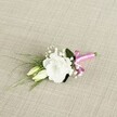 A delicately crafted wedding boutonnière lies at a soft angle on a textured, oatmeal-beige fabric that looks like finely woven linen, its subtle threads catching the light in a cosy, homely way reminiscent of an Oxford townhouse drawing room. At the heart of the arrangement sits a fully open white eustoma bloom, also known as lisianthus, its many ruffled petals layered like fine silk, creating a gentle cup of soft ivory that glows against the neutral background. Just below and to the left, two elongated eustoma buds in creamy pale green rest close to the main flower, their tips still closed, suggesting new beginnings and the quiet anticipation of a wedding morning near Christ Church Meadow or along the River Cherwell. Tiny clouds of white gypsophila, or baby's breath, are threaded through the design, their tiny star-like blossoms giving the piece an airy, romantic feeling. Slender, grass-like blades of deep green foliage sweep gracefully towards the lower left, adding movement and a fresh garden texture, while a slightly broader dark green leaf sits discreetly behind the main bloom, offering depth and contrast. The stems are neatly bound at the base with a vivid fuchsia satin ribbon, tied into a pert, polished bow that introduces a bright, joyful note of colour, like a flash of a bridesmaid's sash in an Oxford college quad. Soft, even lighting highlights each petal edge and leaf vein without harsh shadows, showcasing the care and precision a local florist would use when preparing a groom's buttonhole for a ceremony in central Oxford, from Jericho to Headington, blending classic white-and-green elegance with a playful modern pink accent.