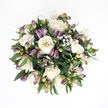 From directly above, this sympathy bouquet appears like a gentle circle of calm placed on a pristine white surface, every detail speaking of care and respect. At its core, several creamy white roses bloom in soft spirals, their petals smooth and velvety to the eye, moving from pure ivory at the outer edges to a delicate hint of peach deep in the centre. Some roses are fully open, serene and composed, while others are more tightly gathered, as if holding their emotions close. Threaded gracefully among them are purple alstroemeria buds, their slender forms carrying a gradient of colour that shifts from deep lavender and plum at the tips to muted green and soft blush at the base. Most of these buds remain closed, suggesting the quiet promise of more beauty to come, with just a few starting to reveal faint striations inside. Tiny sprays of white baby's breath float around the roses and alstroemeria like a light mist, creating pockets of softness and breathing room, much like the peaceful spaces you find walking along the River Cherwell. A collar of rich, deep green foliage surrounds the blooms, the leaves broad, polished, and gently curving, giving the arrangement structure and a subtle sense of embrace. The bouquet is compact yet not crowded, forming a harmonious, spherical shape that feels both dignified and soothing. It's the sort of floral gesture you might send to a home in Headington, Marston, or the heart of Oxford as a tender expression of sympathy, offering quiet support and a touch of natural beauty during a difficult time.