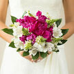 This image shows a hand-tied bridal bouquet that blends modern confidence with traditional romance, set against soft natural light that feels very much like an Oxford afternoon. At its heart, magenta peonies sit in a plush cluster, their generous, layered petals unfolding in ruffles that look almost cloud-soft, the deep tones giving the bouquet a sense of bold character. Around them, white alstroemeria form a gentle ring, each bloom marked with fine, painterly streaks that add detail and draw the eye closer, softening the drama of the peonies while keeping the whole design refined and elegant. Threaded throughout are slim spikes of pale green buds and new shoots, like tiny promises of beginnings yet to come, offering height and a fresh, airy rhythm so the bouquet doesn't feel still or static. Supporting foliage in cool, rich greens encases the flowers, strong yet graceful, with broad leaves that hint at a fresh, garden-like scent-something you might associate with early walks along the river near Christ Church Meadow in late spring. The play of light across the petals adds depth, catching the silky sheen of the peonies and the almost translucent edges of the alstroemeria, creating shadows that give the bouquet a sculpted, three-dimensional presence. Held gently in bridal hands, the flowers seem to glow against the suggestion of a creamy gown, capturing that intimate moment before stepping into a ceremony tucked away in an Oxfordshire church or city venue. The bouquet feels personal and heartfelt, a carefully crafted piece designed by a local florist who understands how flowers can give quiet voice to love, hope, and cherished milestones.