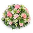 A soft, dome-shaped tribute of closely packed blooms, arranged with the quiet care of an experienced florist and set against a clean white backdrop. At the heart of the composition are classic pink roses in varying scales and tones - from a richer salmon-pink in the larger, fully opened heads to delicate pastel blush in smaller spray roses - their velvety petals layered in graceful spirals that invite a gentle touch. Nestled between the roses are clusters of pure white freesia, some with their bell-shaped corollas fully unfurled to reveal pale yellow stamens, others still in tight, conical buds that promise unfolding fragrance over the coming days. The overall texture is lush and cushion-like: glossy deep-green leaves (think Ruscus or Salal) form a steady, verdant backdrop while smaller, cream-edged variegated leaves - likely pittosporum - catch the light and add a soft contrast that keeps the palette airy rather than heavy. No stems are visible; the arrangement reads as a single, comforting mass of flowers and foliage, meticulously wired or foam-set for a formal, rounded silhouette. Natural, diffuse daylight gently lifts the colours - the pinks feel warm without being bright, and the whites read as calm and pure - creating a soothing presence suited to a memorial or quiet celebration of life. Imagine this piece delivered to a family home near University Parks or placed on a chapel table in Jericho: it speaks of tenderness, restraint, and a florist's skill in balancing scent, colour, and form for moments of remembrance.
