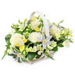 The photograph shows a serene and elegant funeral flower basket arranged in a light, airy style that would feel at home in many of Oxford's peaceful memorial spaces. The basket is crafted from pale woven wicker in a soft beige or off-white tone, with a matching handle that rises in a gentle arc over the centre, echoing the curve of old stone bridges over the Thames. Nestled inside, the flowers create a rounded, abundant display that just fills the rim without appearing overcrowded. Large, fully opened roses in creamy white form the main focal points, their velvety petals unfolding in generous layers that suggest tenderness and respect. Interspersed with the roses are delicate, star-shaped clematis blossoms, their petals painted in soft lavender and pale periwinkle hues, each centred with a tiny burst of yellow-green that adds a light, almost celestial sparkle. Around and between these feature flowers, groups of freesia-like blooms in white and pale lemon note contribute a gently ruffled texture and a sense of soft fragrance, with a mix of open flowers and tight buds that hint at the passage of time. Additional white filler flowers, possibly lisianthus or similar, fill out the composition without overpowering it. The entire arrangement is wrapped in a generous layer of foliage, with deep, glossy dark green leaves and slender, lighter green stems providing contrast and depth, much like a shaded corner in University Parks. The mood of the arrangement is calm, dignified, and compassionate, making it well-suited for funerals, memorial services, or condolence deliveries to homes across Oxford, where it can sit quietly as a symbol of comfort, remembrance, and gentle support.