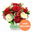 A festive and romantic floral arrangement is shown in crisp detail against a plain white background, allowing the rich colours of the bouquet to take centre stage. At its core are abundant red roses, fully opened with velvety petals spiralling outward, paired with equally generous white roses in a soft, creamy hue. The contrast between crimson and ivory feels both timeless and celebratory, like a table set for a special dinner in an Oxford townhouse near the High Street or along Banbury Road. Fine clusters of bright red filler flowers weave through the roses, creating a lacy, mist-like layer that lightens the composition and evokes the delicacy of baby's breath, only in bold scarlet. Glossy, round hypericum berries in deep red are tucked between the blooms, offering a textured, berry-like accent that hints at winter festivities and cosy gatherings. Around the edges and peeking through the centre, green foliage and eucalyptus leaves lend movement and freshness, their varied shades of green and silvery-blue catching subtle reflections of light. The bouquet is set in a modern rectangular glass vase, crystal clear so the stems are visible, lined up in tidy verticals that echo the neat, structured style often favoured in local Oxford offices and riverside apartments. A green and white gingham ribbon hugs the middle of the vase, its checked pattern adding a gentle countryside character that feels right at home in Oxfordshire. In the lower right of the picture, an orange circular badge with white text reading VASE INCLUDED signals that the arrangement is ready to place straight onto a dining table, reception desk, or bedside, perfect for anniversaries, romantic surprises, or simply sending love across the city.